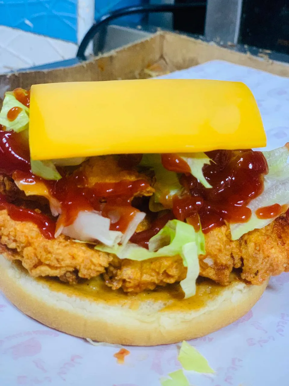 Fried chicken burger topped with a slice of cheddar and ketchup